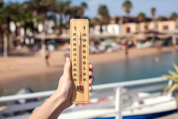 Mano de mujer sostiene termómetro en el fondo de la playa. Concepto de verano, clima y clima - Foto, Imagen