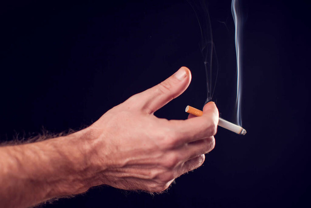 Cigarrillo en mano sobre fondo negro. Concepto de adicción al humo - Foto, imagen