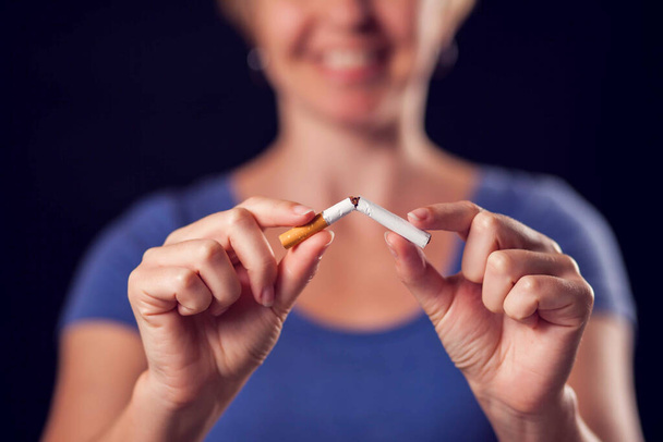 Woman in a blue t-shirt holding broken cigarette in hands. Stop smoking concept - Photo, Image