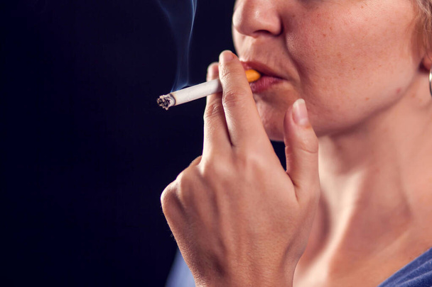 Femme fume cigarette sur fond noir. Concept de dépendance au tabac - Photo, image