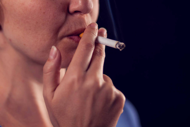 Kobieta pali papierosa na czarnym tle. Koncepcja uzależnienia od tytoniu - Zdjęcie, obraz