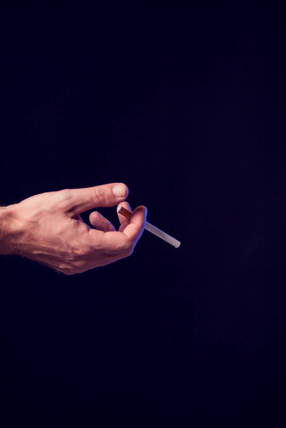 Sigaret in de hand op zwarte achtergrond. Begrip rookverslaving - Foto, afbeelding