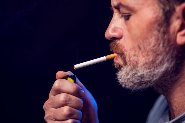Portret mężczyzny pali papierosa na czarnym tle. Koncepcja uzależnienia od tytoniu - Zdjęcie, obraz
