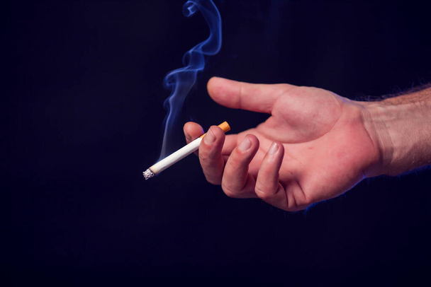 Сигарета в руке на черном фоне. Концепция дымовой зависимости - Фото, изображение