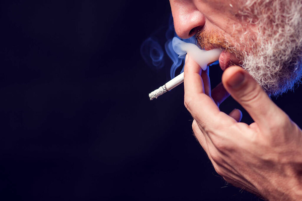 Siyah arka planda sigara içen bir adamın portresi. Tütün bağımlılığı konsepti - Fotoğraf, Görsel