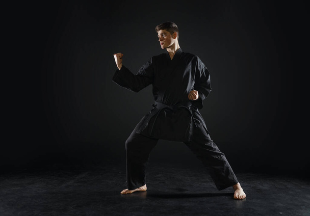 Siyah kimonolu erkek karate dövüşçüsü, dövüş duruşu, karanlık bir geçmişi var. Antrenmanlı adam, dövüş sanatları. - Fotoğraf, Görsel