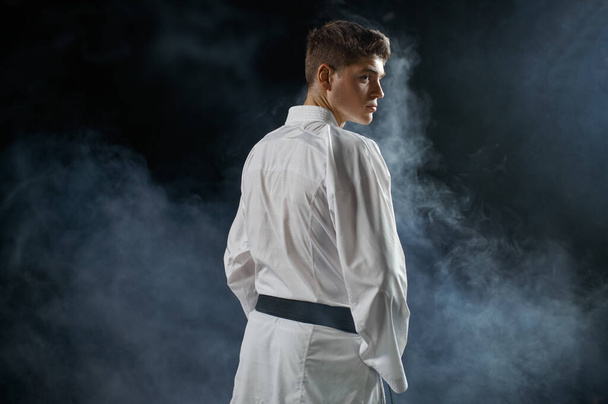 Karateka masculino, lutador com faixa preta, visão traseira, fundo escuro. Homem no treino de karatê, artes marciais, treinamento antes de lutar contra a concorrência - Foto, Imagem