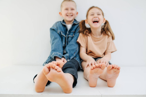 Cheerful little siblings sitting on a table with bare feet. Both laughing. - Fotó, kép