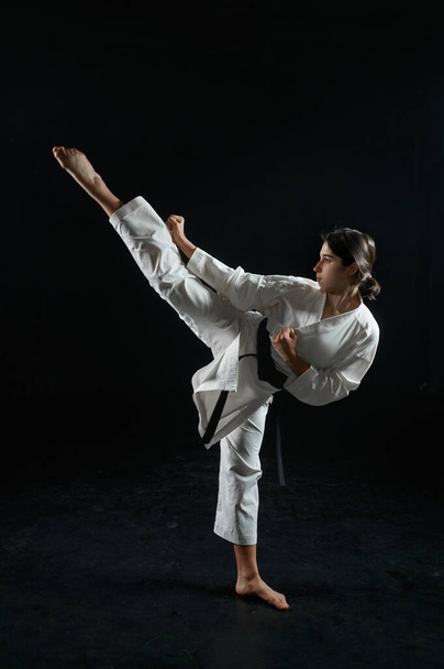 female karate fighter in white kimono, combat stance in action, dark background. Karateka on workout, martial arts, training before fighting competition - Photo, Image
