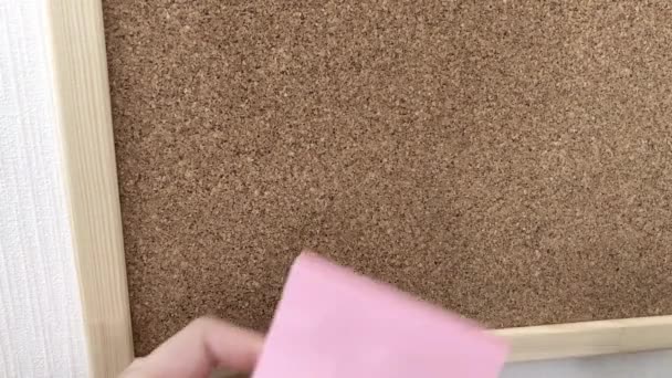 Joven mujer pega papel rosa para una nota a un tablero de corcho. - Metraje, vídeo