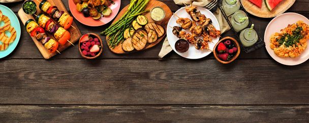 Healthy plant based summer bbq top border. Above view over a dark wood banner background. Grilled fruit and vegetables, skewers, cauliflower steak and vegetarian sides. Copy space. - Photo, Image