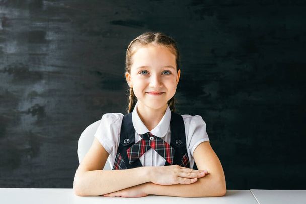 Portrait beautiful positive little schoolgirl sitting at her desk. Back to school concept. - Fotó, kép