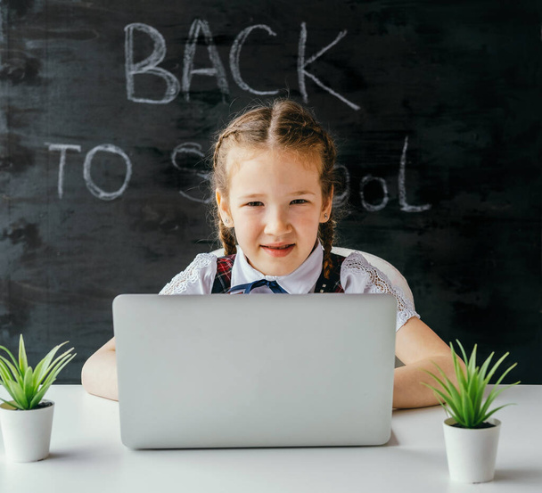 Cute little school girl sitting at the desk and using computer. Back to school and online lessons concept. - Foto, Imagem
