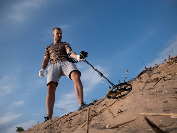 Парень на песчаной земле с металлоискателем ищет сокровища в солнечный летний день - Фото, изображение