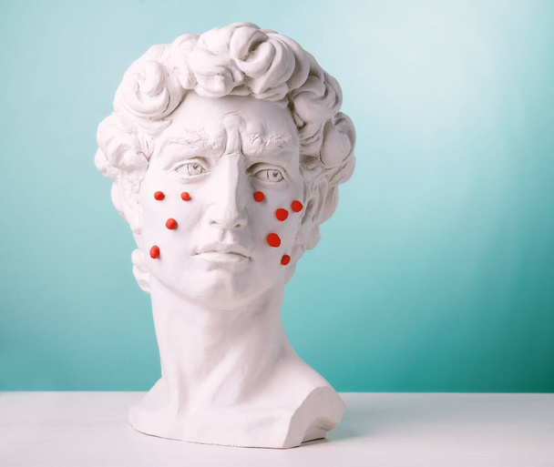 Plaster head statue with red pimples made of plasticine.Problem skin concept on blue background. - Φωτογραφία, εικόνα