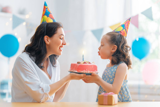 The kid is blowing out the candles on the cake. Mother and daughter are celebrating birthday. - Photo, image