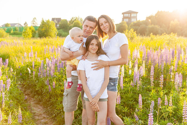 屋外で子供を受け入れる幸せな家族の母親の父親。背景に花を咲かせる夏野の女男赤ちゃんと10代の女の子。幸せな家族のお父さんと娘再生上の牧草地 - 写真・画像
