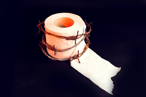 Toilet paper with barbed wire around it on black background. People, healthcare and medicine concept. - Photo, Image