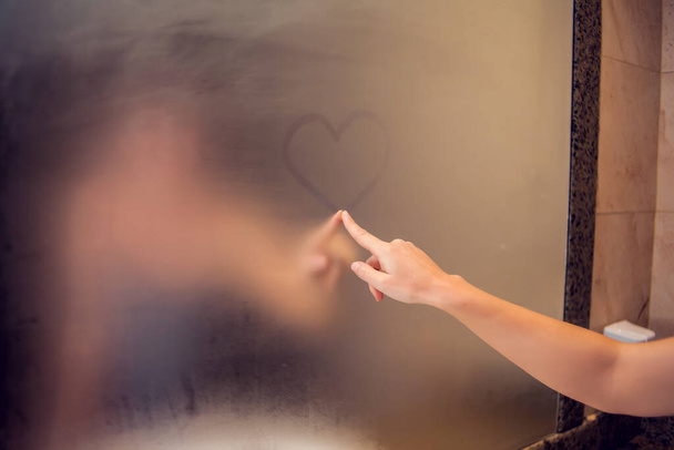 Bir kadın aynaya kalp çizer. Kalp, banyodaki bardakta parmak izidir. İnsanlar ve yaşam tarzı kavramı - Fotoğraf, Görsel