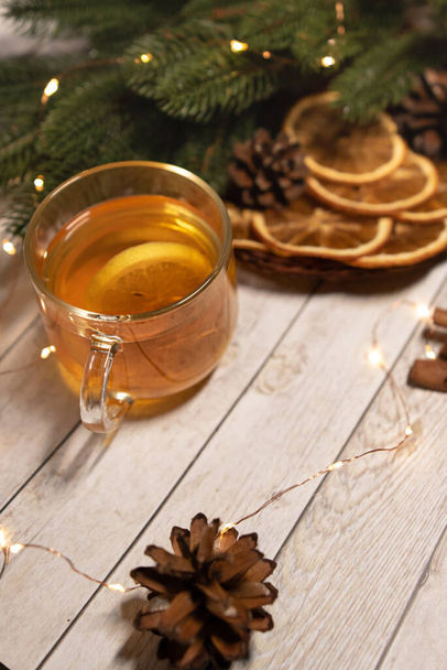 una taza de té caliente de Navidad con limón sobre una madera clara. sobre el fondo de un asterisco anís estrellado, una naranja y una ramita de un árbol de Navidad. concepto de Navidad - Foto, Imagen