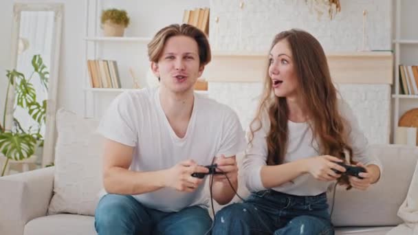 Caucasian married couple friends young woman and millennial man sitting at home couch playing video game console using joysticks controllers shouting from competition guy prevents girl from winning - Footage, Video