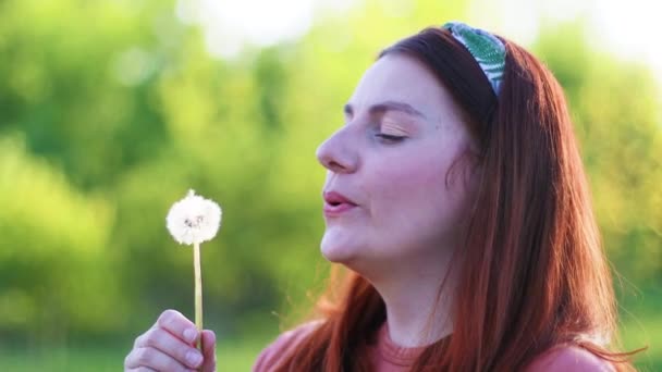 Καυκάσια χιλιετή γυναίκα φυσάει αγριολούλουδα σε εξωτερικούς χώρους - Πλάνα, βίντεο