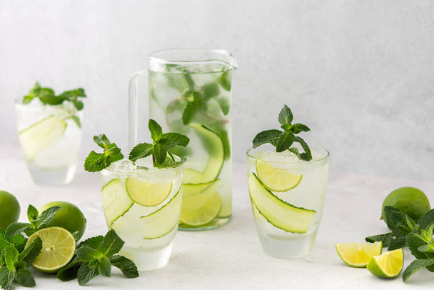 Κρύα δροσιστικά ποτά με λάιμ και αγγούρι, καλοκαιρινό παγωμένο ρόφημα και φρέσκια πράσινη μέντα, κανάτα με λεμόνι - Φωτογραφία, εικόνα