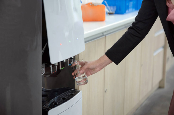 Mulher mão segurando vidro enchendo água fria do dispensador de água - Foto, Imagem