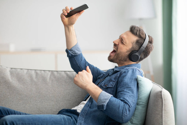 Ecstatic bearded man singing songs, using smartphone and headset - 写真・画像
