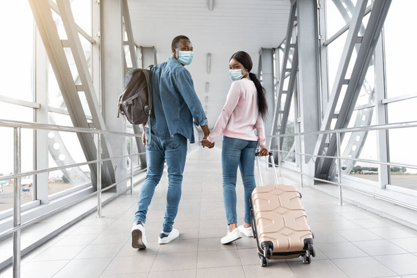 Voyages pendant le coronavirus. Couple noir dans les masques médicaux marchant dans le terminal de l'aéroport - Photo, image