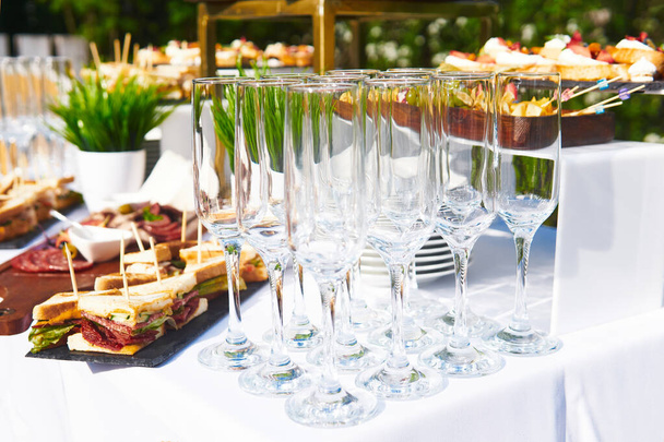 buffet ao ar livre - copos vazios no fundo de lanches frios na mesa à espera de convidados - Foto, Imagem