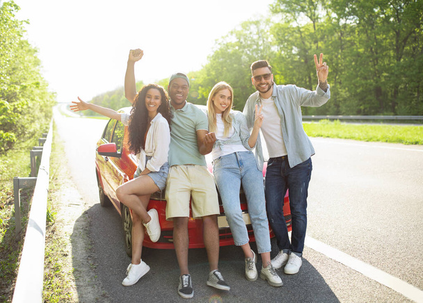 Retrato de amigos felices y diversos posando cerca de su coche en la carretera, haciendo diferentes gestos, sonriendo a la cámara - Foto, Imagen