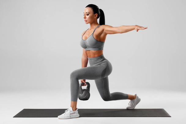 Αθλητικό κορίτσι κάνει ασκήσεις με κέτλμπελ, προπόνηση μυών ποδιών. Fitness γυναίκα κάνει μπροστά ένα πόδι βήμα lunge - Φωτογραφία, εικόνα