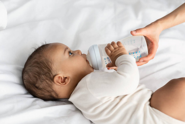 Милый маленький афроамериканец, пьющий из детской бутылочки - Фото, изображение