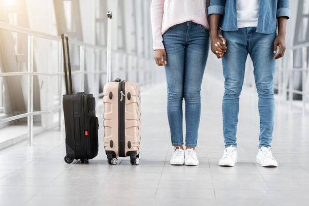 Gemeinsam reisen. Schwarzes Paar hält Händchen, während es im Flughafenkorridor steht, beschnitten - Foto, Bild