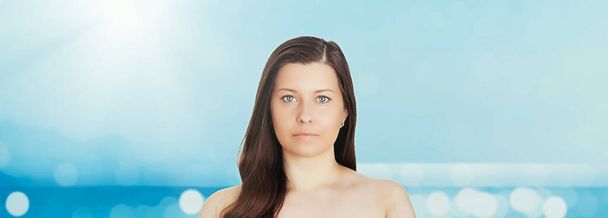 Cuidado de la piel y protección solar en verano. Retrato de una hermosa joven bronceada, azul mar y cielo sobre fondo, belleza, bienestar y concepto de viaje - Foto, imagen