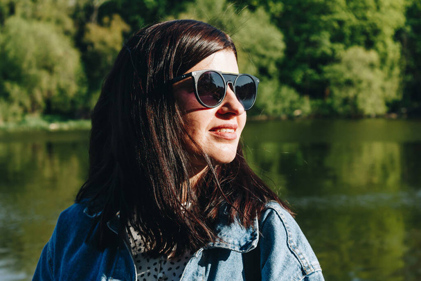 Porträt einer brünetten Frau mit Sonnenbrille und Jeansjacke - Foto, Bild