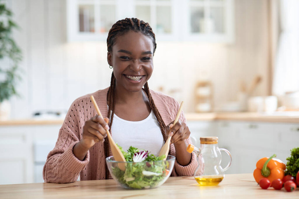 Feliz sonriente mujer afroamericana preparando ensalada de verduras frescas en la cocina - Foto, imagen