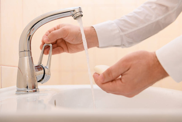 lavado de manos con jabón o gel bajo el agua corriente en el lavabo, limpieza e higiene, manos de hombre vestidas con una camisa blanca - Foto, Imagen