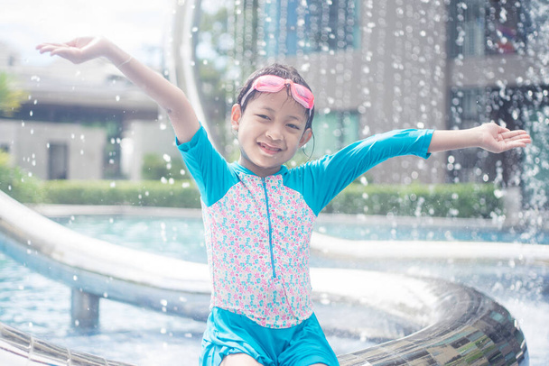 Smiling asian little girl is wearing sunglasses in water park in summer time - Photo, Image