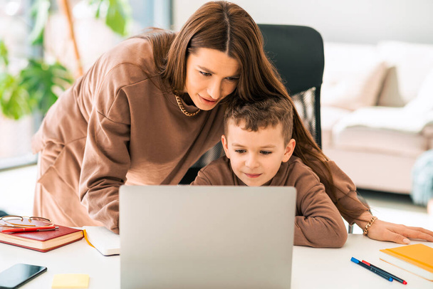 Anya segít a kisfiának az online házi feladatban a laptopon. Távolsági oktatás - Fotó, kép