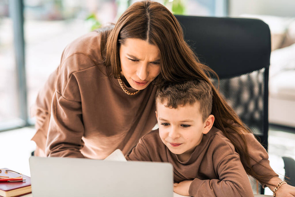 Mutter hilft ihrem kleinen Sohn bei Online-Hausaufgaben am Laptop. Fernstudium - Foto, Bild