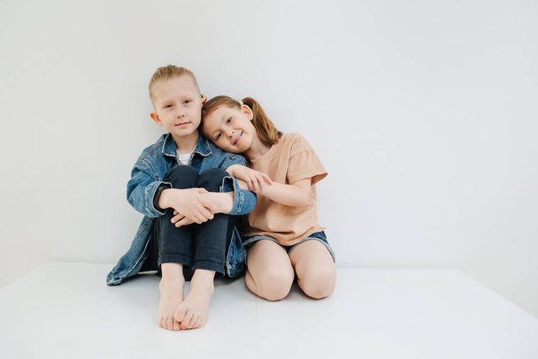 Adorable little siblings sitting on a table next to each other. Head on shoulder - Fotografie, Obrázek