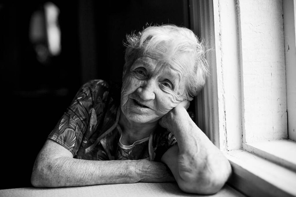 Portrait of old woman sitting in her home. Black and white photo. - Fotoğraf, Görsel
