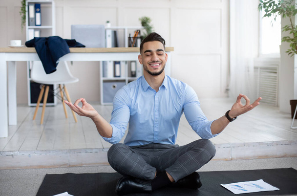 職場のストレス管理の概念。穏やかなアラブ人男性瞑想で目を閉じて、ヨガをします現代オフィス - 写真・画像