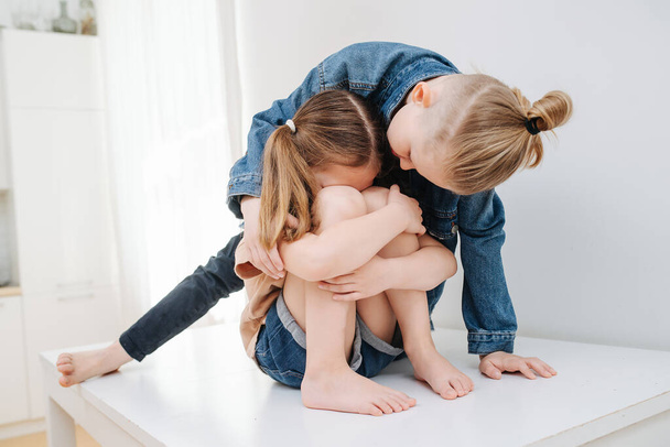Crying little girl sitting on a table. Her brother trying to calm her down. - Fotoğraf, Görsel