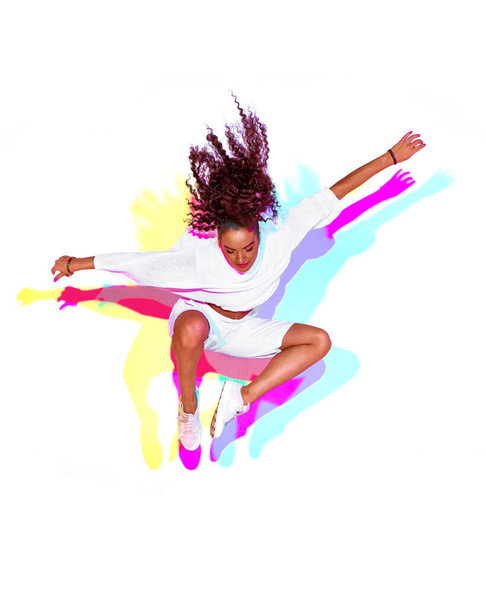 Jumping stylish mixed race young girl on white background. Rainbow colourful studio light. Fiery hip hop dance leap - Фото, зображення