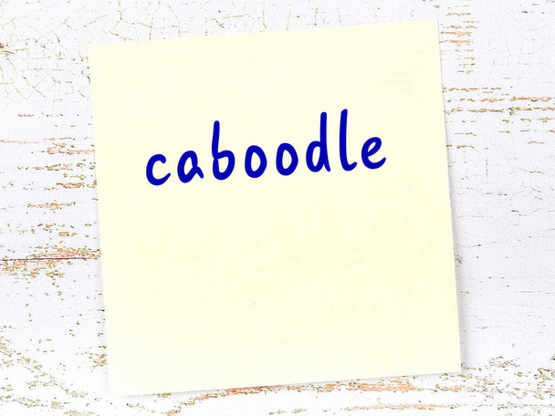 Herinnering aan Caboodle. Geel plakkerig velletje papier op houten muur met inscriptie - Foto, afbeelding