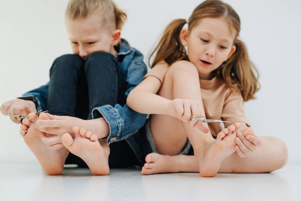 Funny kids. Little siblings with bare feet clipping nails on their toes. - Фото, изображение