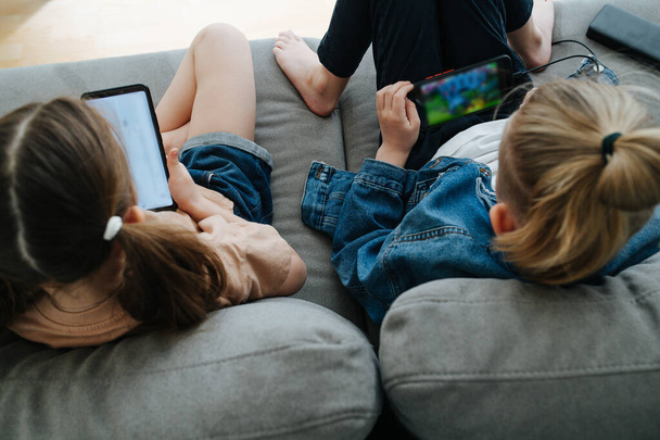 Two siblings sitting on the couch, watching their phones next to each other - Foto, afbeelding